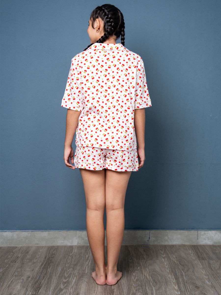 Person wearing a white shirt with red patterns and matching shorts against a blue wall.