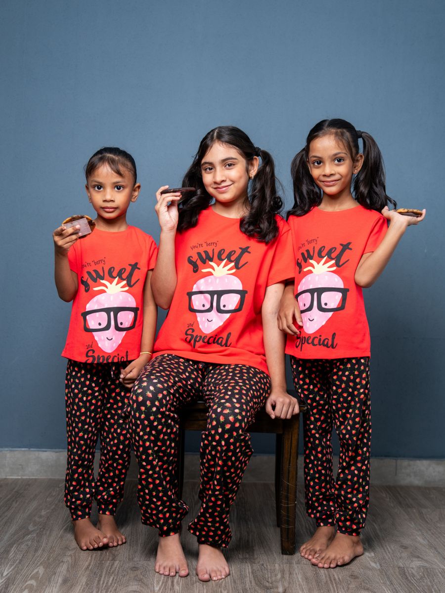 Three children wearing matching red shirts and black polka dot pants against a blue wall.