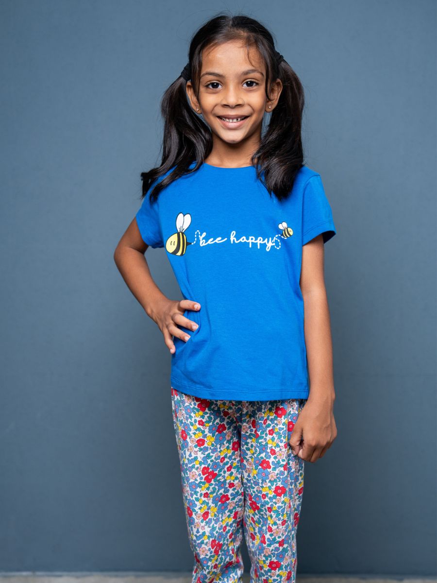 Young girl wearing a blue t-shirt with bee graphics and text, standing against a gray background