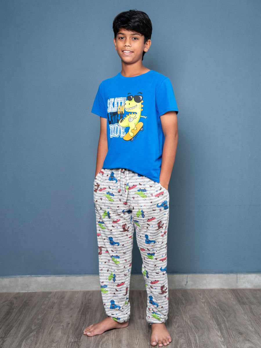 Young boy wearing a blue t-shirt with a graphic design and patterned pajama pants against a gray wall.