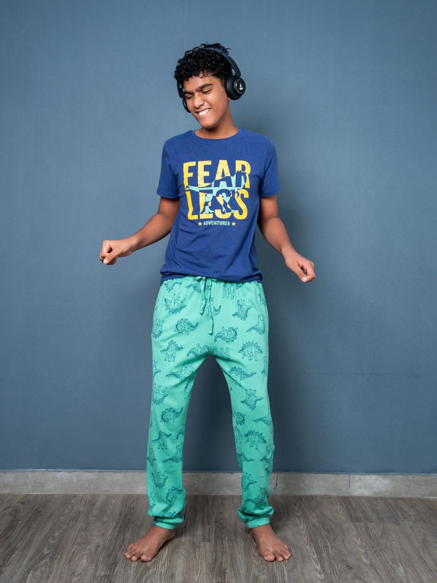 Person wearing a blue t-shirt with text and green patterned pants against a blue wall.