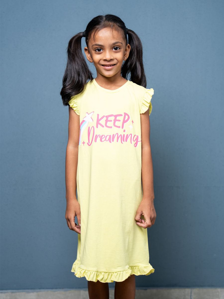 Young girl wearing a yellow dress with ‘Keep Dreaming’ text against a blue background