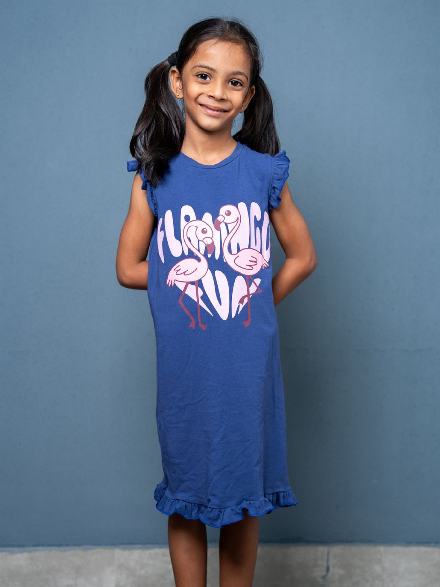 Young girl wearing a blue dress with flamingo design against a gray background