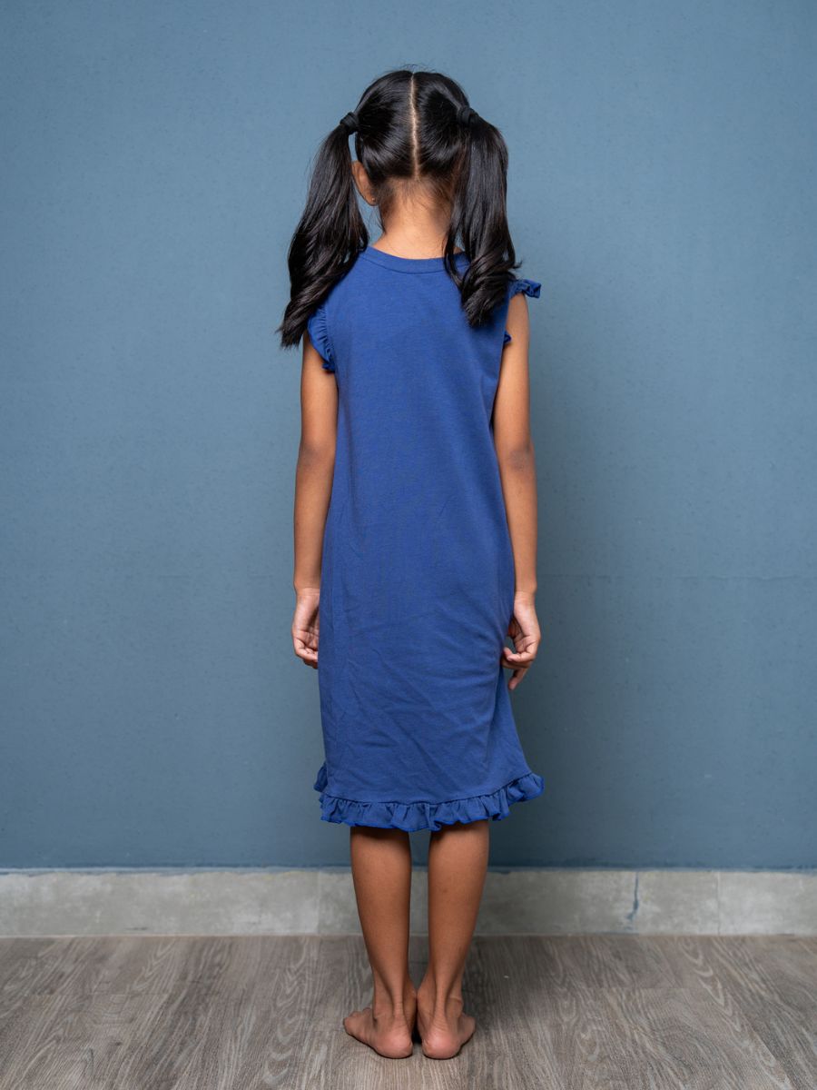 Young girl wearing a blue dress standing against a plain blue wall.