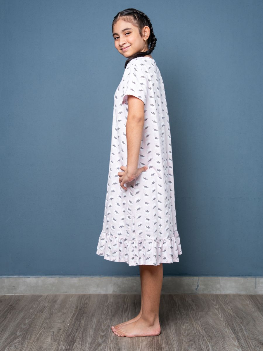 Young girl wearing a white dress with a pattern against a blue wall.
