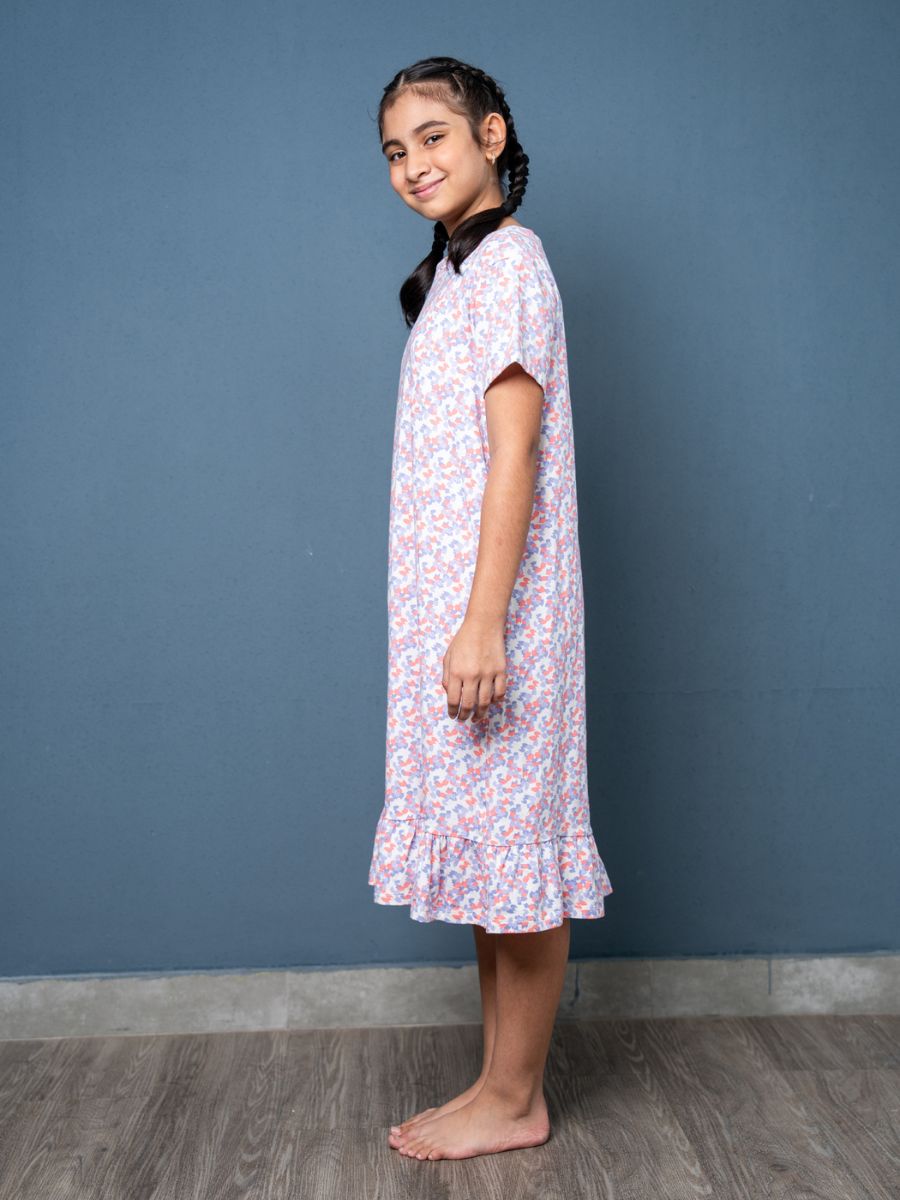 Young girl wearing a floral nightgown against a blue wall.