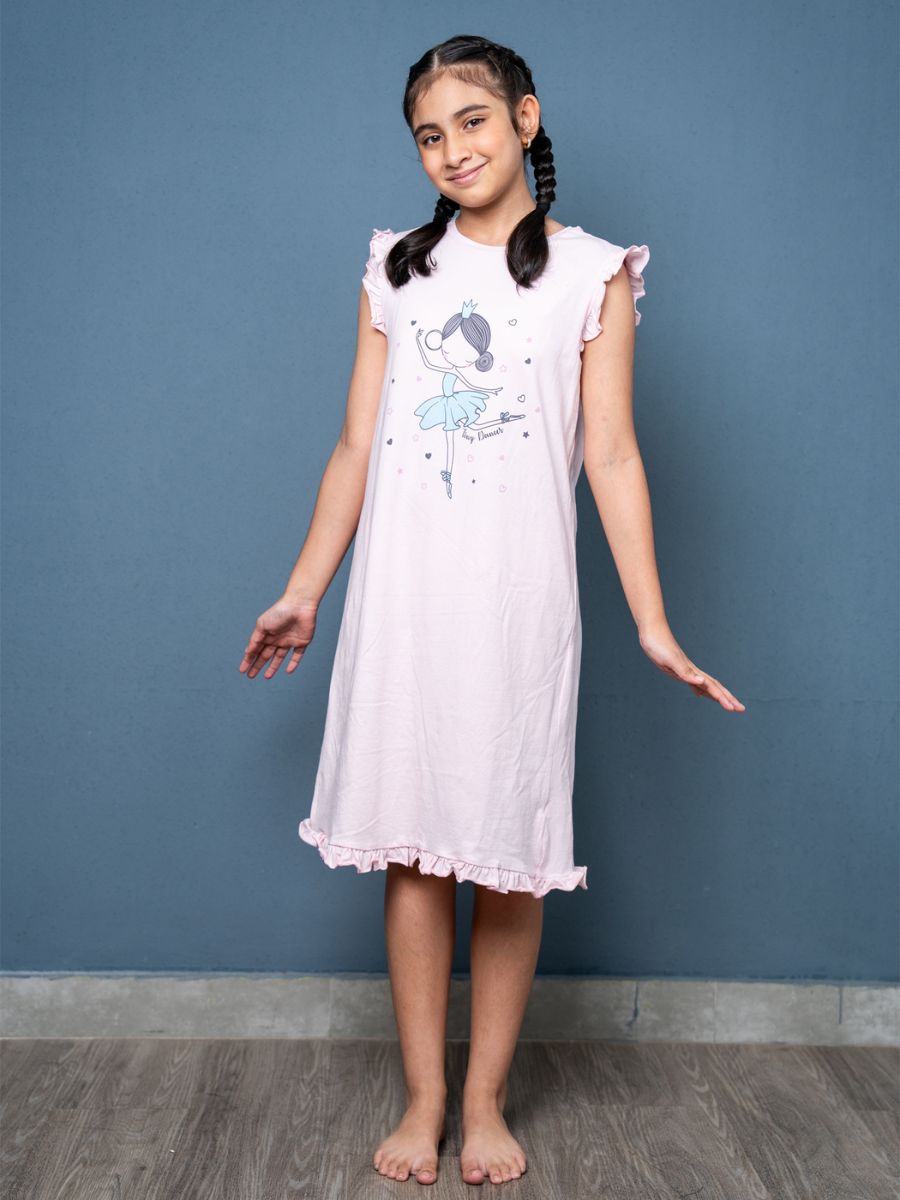Young girl wearing a lilac nightgown with a cartoon design against a blue wall.