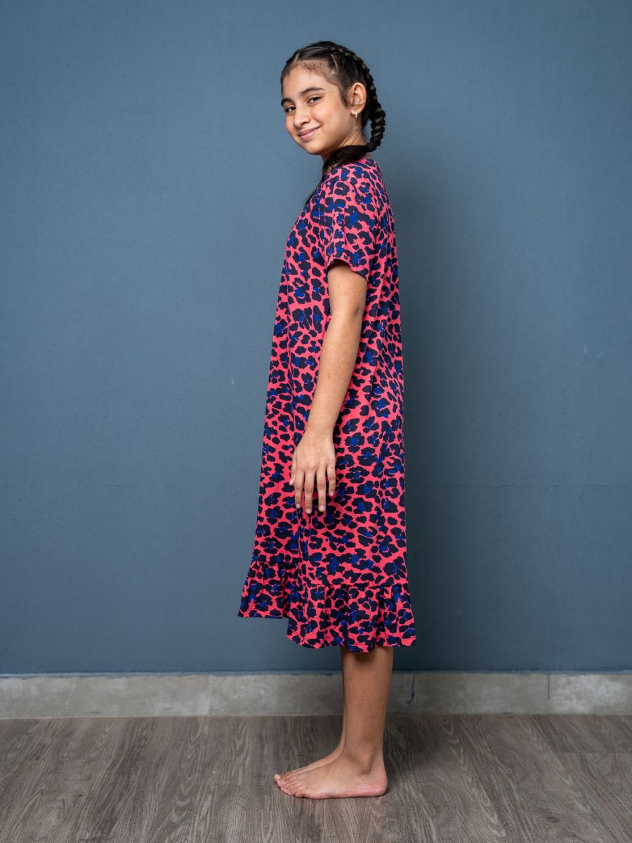 Girl wearing a pink and blue patterned dress against a blue wall.
